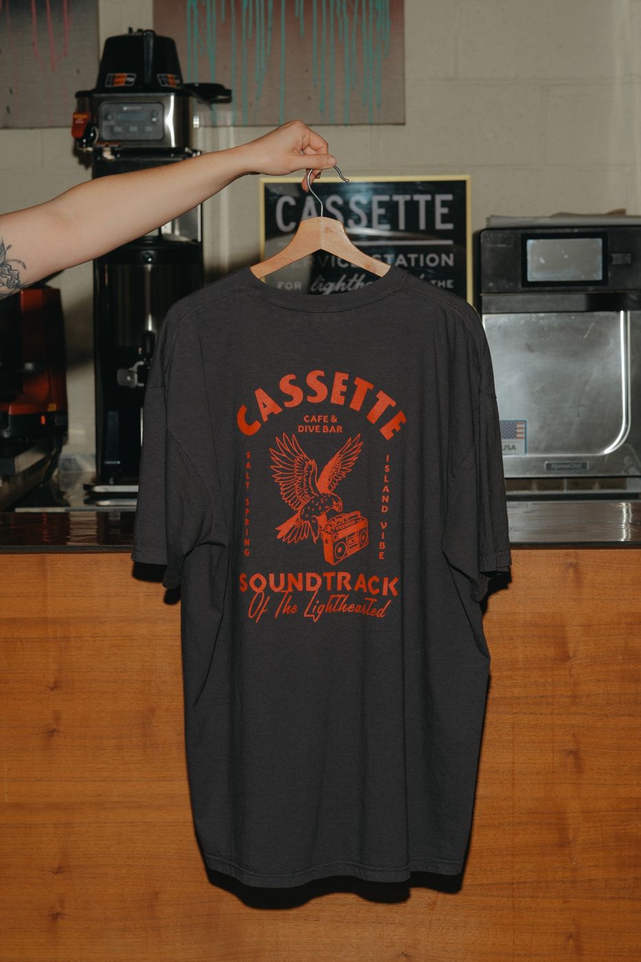 A Cassette Soundtrack of the Lighthearted T-shirt held up at the cafe counter